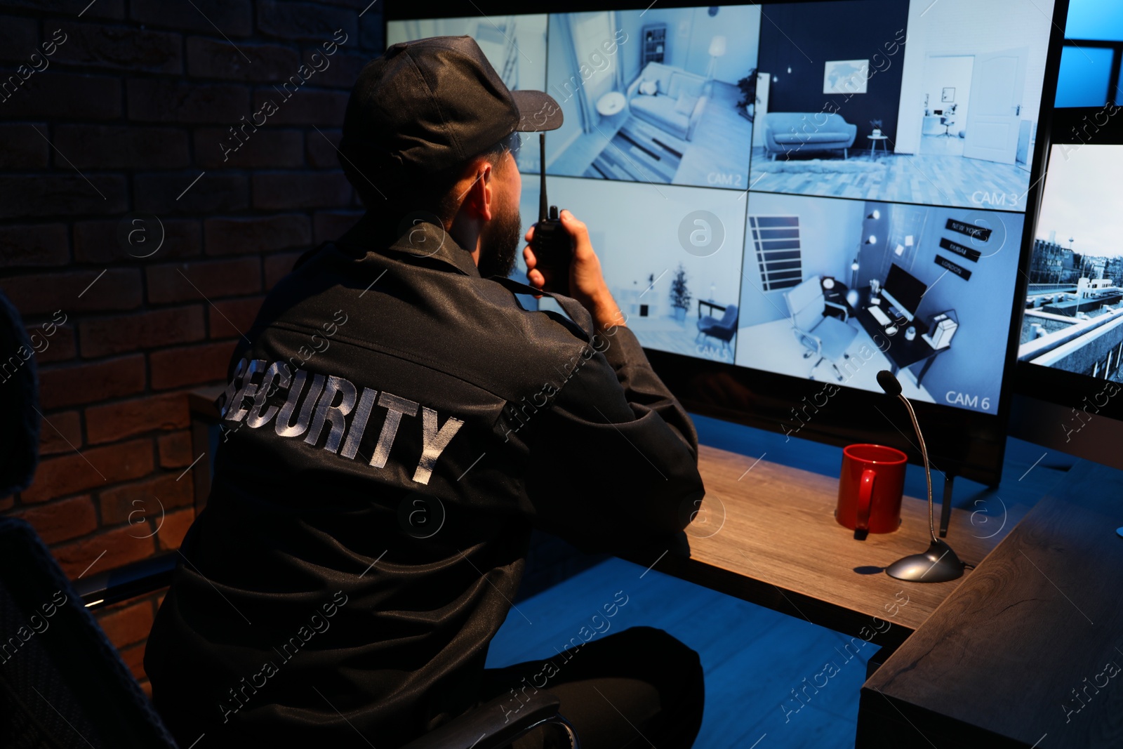 Photo of Security guard monitoring CCTV cameras in office at night, back view