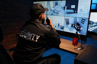 Photo of Security guard monitoring CCTV cameras in office at night, back view