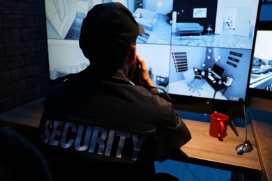 Photo of Security guard monitoring CCTV cameras in office at night, back view