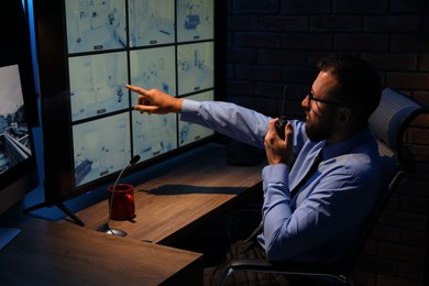 Photo of Security guard monitoring CCTV cameras and using walkie talkie in office at night