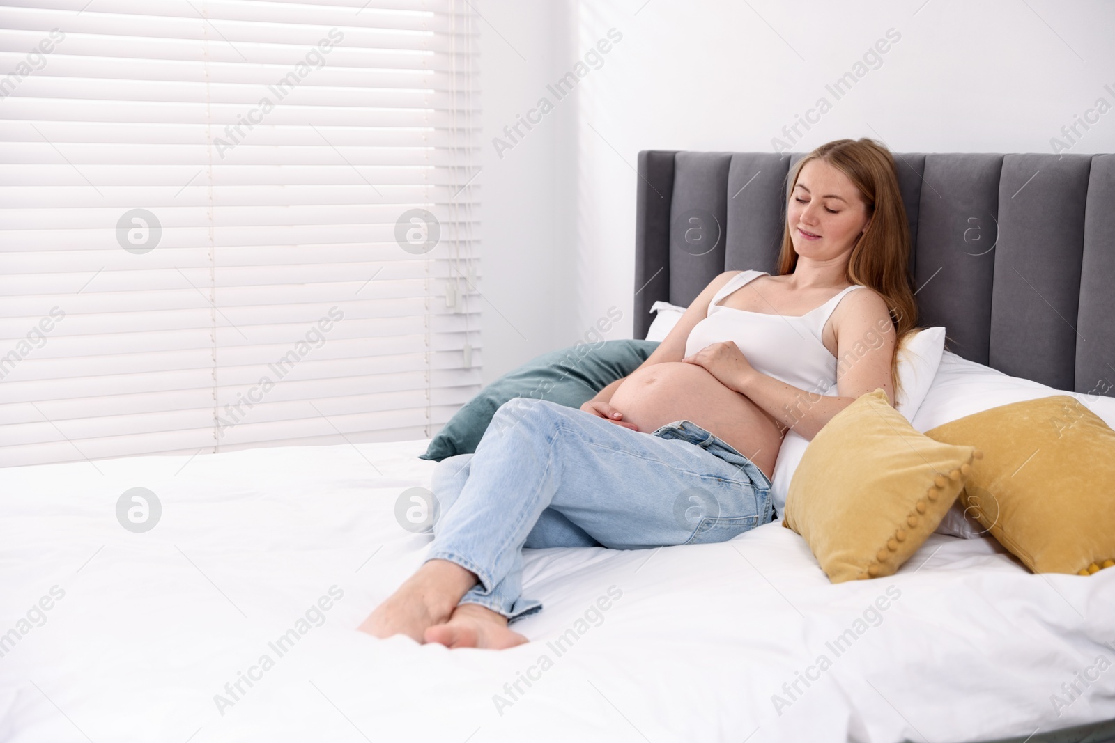 Photo of Beautiful pregnant woman on bed at home. Space for text