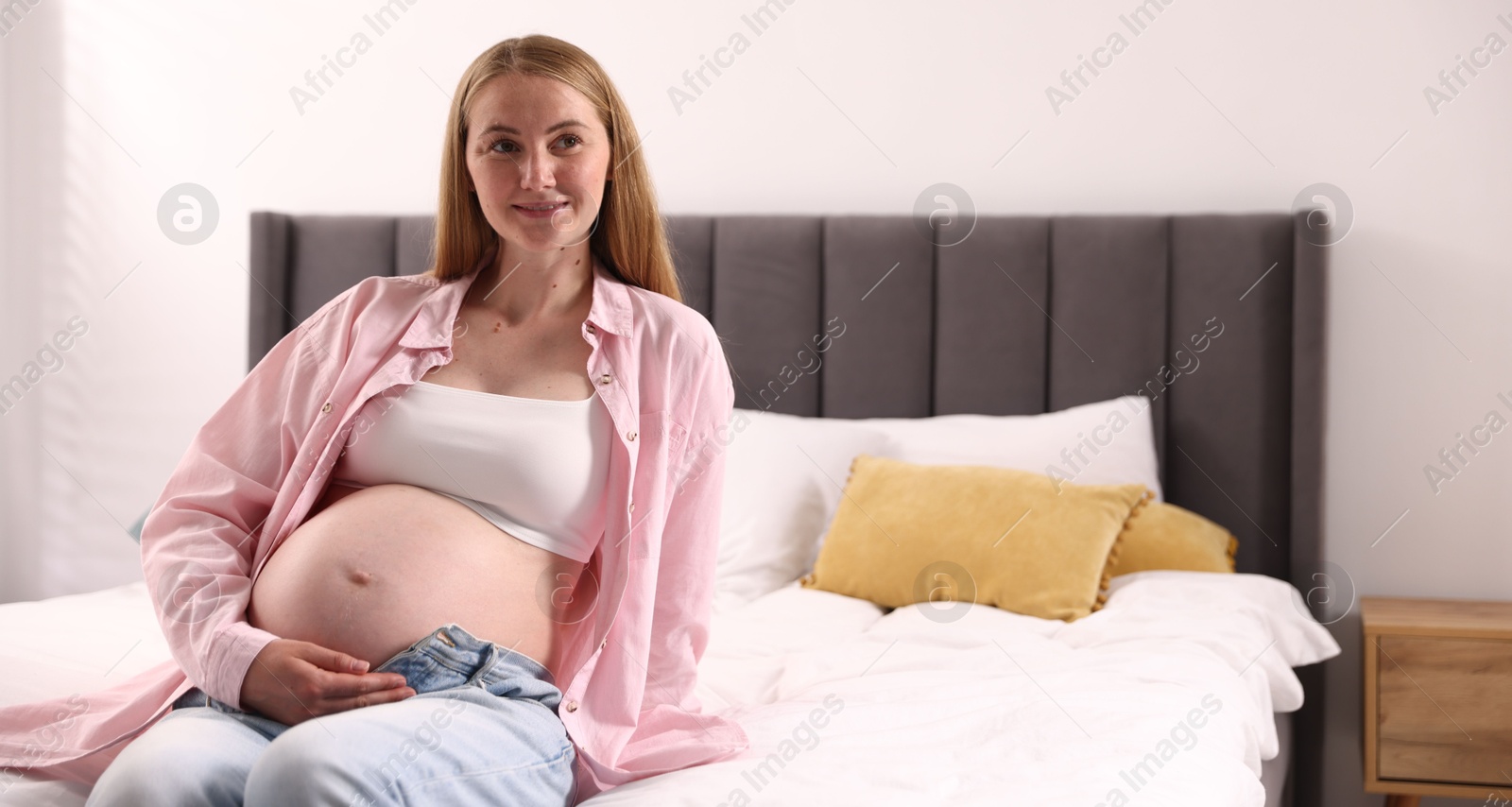 Photo of Beautiful pregnant woman on bed at home. Space for text