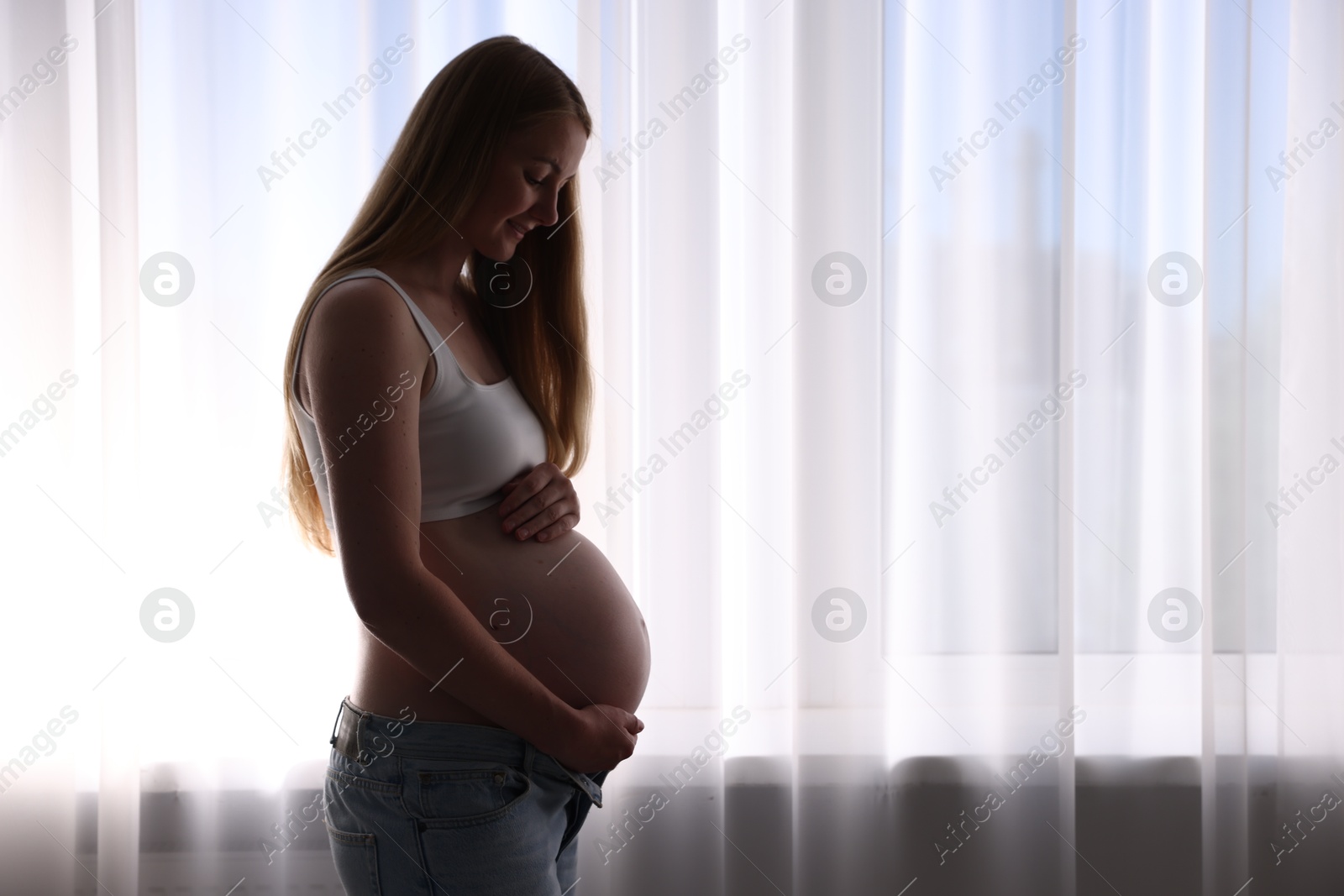 Photo of Beautiful pregnant woman near window at home. Space for text