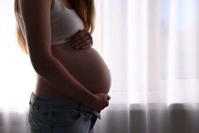 Photo of Beautiful pregnant woman near window at home, closeup