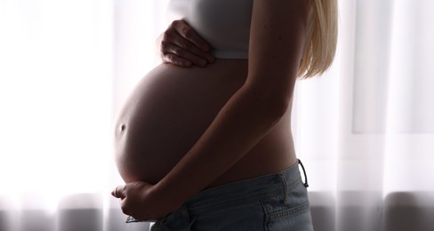 Photo of Beautiful pregnant woman near window at home, closeup
