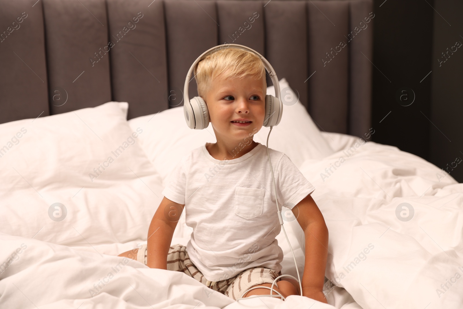Cute little boy in headphones on bed Photo of Cute little boy in headphones on bed