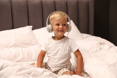 Photo of Cute little boy in headphones on bed