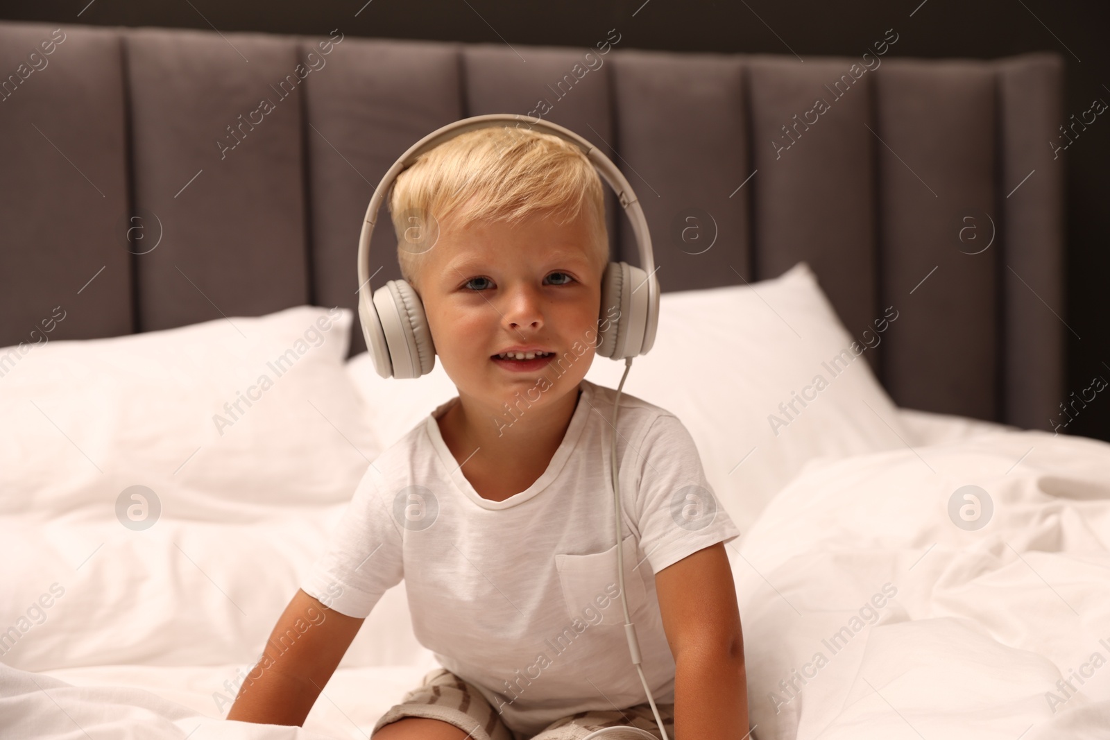 Cute little boy in headphones on bed Photo of Cute little boy in headphones on bed