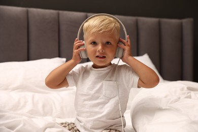 Photo of Cute little boy in headphones on bed