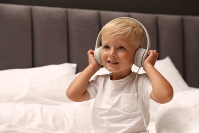 Photo of Cute little boy in headphones on bed