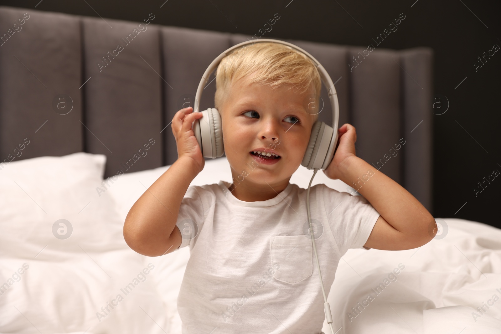 Cute little boy in headphones on bed Photo of Cute little boy in headphones on bed