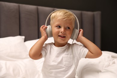 Photo of Cute little boy in headphones on bed