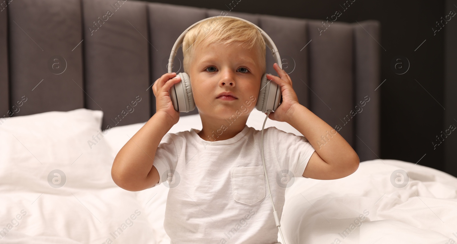 Cute little boy in headphones on bed Photo of Cute little boy in headphones on bed