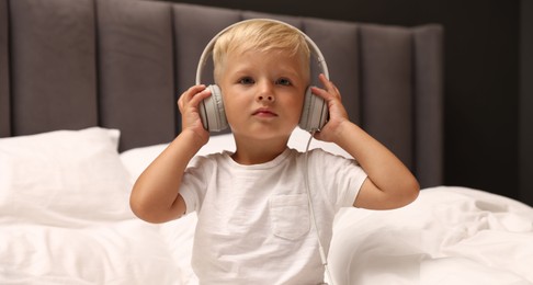 Photo of Cute little boy in headphones on bed