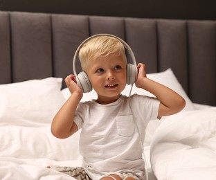 Photo of Cute little boy in headphones on bed