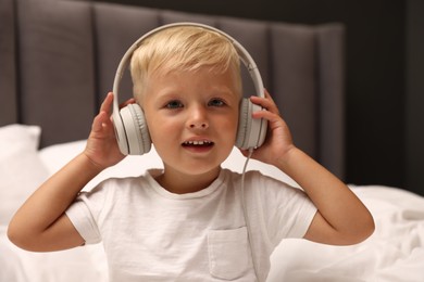 Photo of Cute little boy in headphones on bed