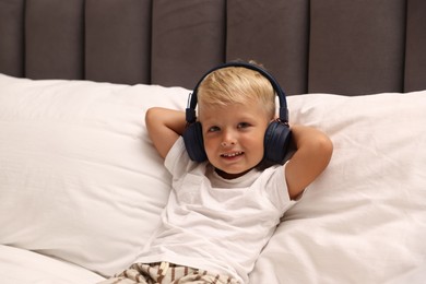 Photo of Cute little boy in headphones on bed