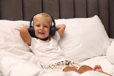 Photo of Cute little boy in headphones on bed