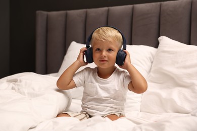 Photo of Cute little boy in headphones on bed