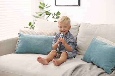 Photo of Cute little boy with microphone on sofa at home