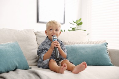 Photo of Cute little boy with microphone on sofa at home