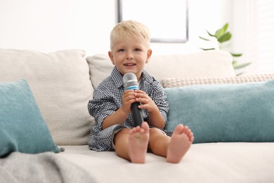 Photo of Cute little boy with microphone on sofa at home