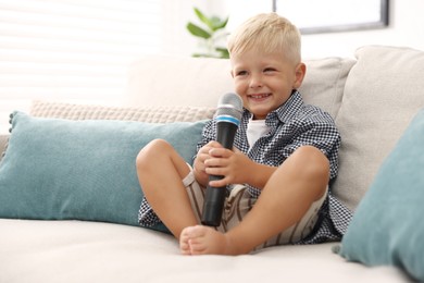 Photo of Cute little boy with microphone on sofa at home