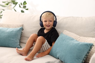 Photo of Cute little boy in headphones on sofa at home