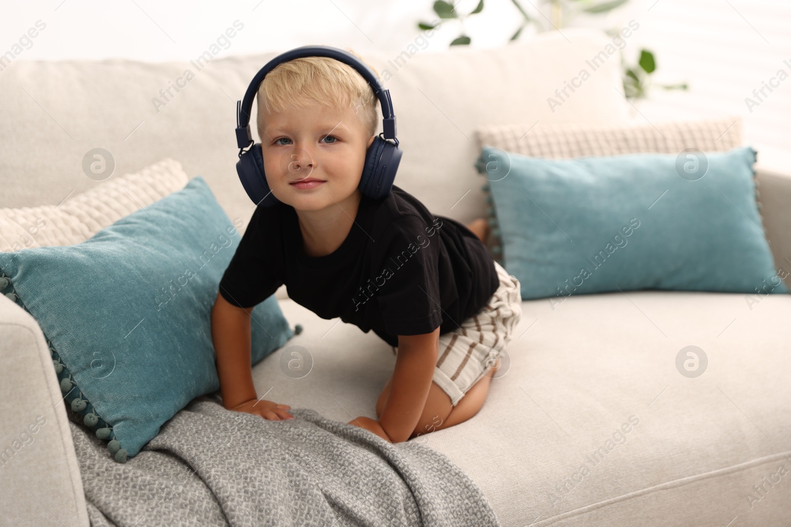 Cute little boy in headphones on sofa at home Photo of Cute little boy in headphones on sofa at home