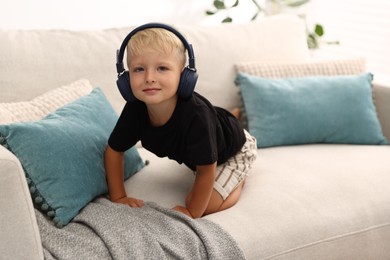 Photo of Cute little boy in headphones on sofa at home