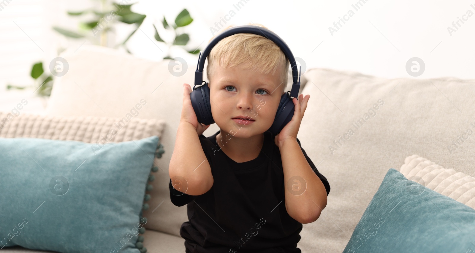 Cute little boy in headphones on sofa at home Photo of Cute little boy in headphones on sofa at home