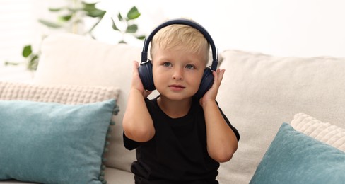Photo of Cute little boy in headphones on sofa at home