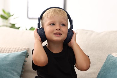 Photo of Cute little boy in headphones on sofa at home