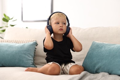 Photo of Cute little boy in headphones on sofa at home