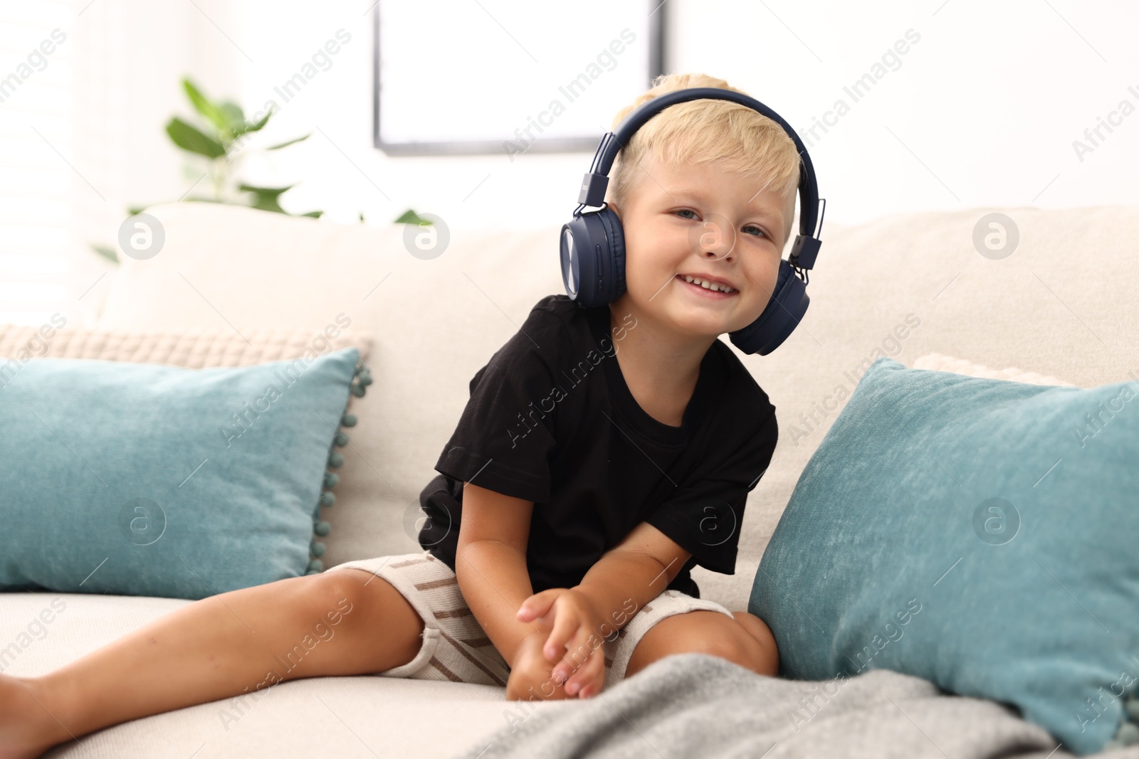 Photo of Cute little boy in headphones on sofa at home