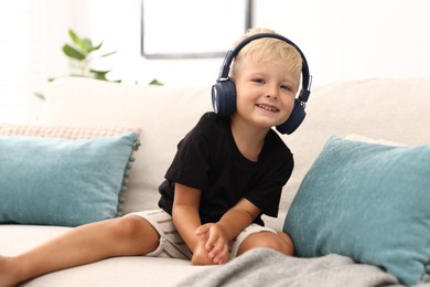 Photo of Cute little boy in headphones on sofa at home