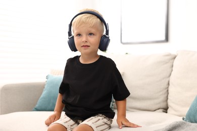 Photo of Cute little boy in headphones on sofa at home