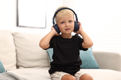 Photo of Cute little boy in headphones on sofa at home