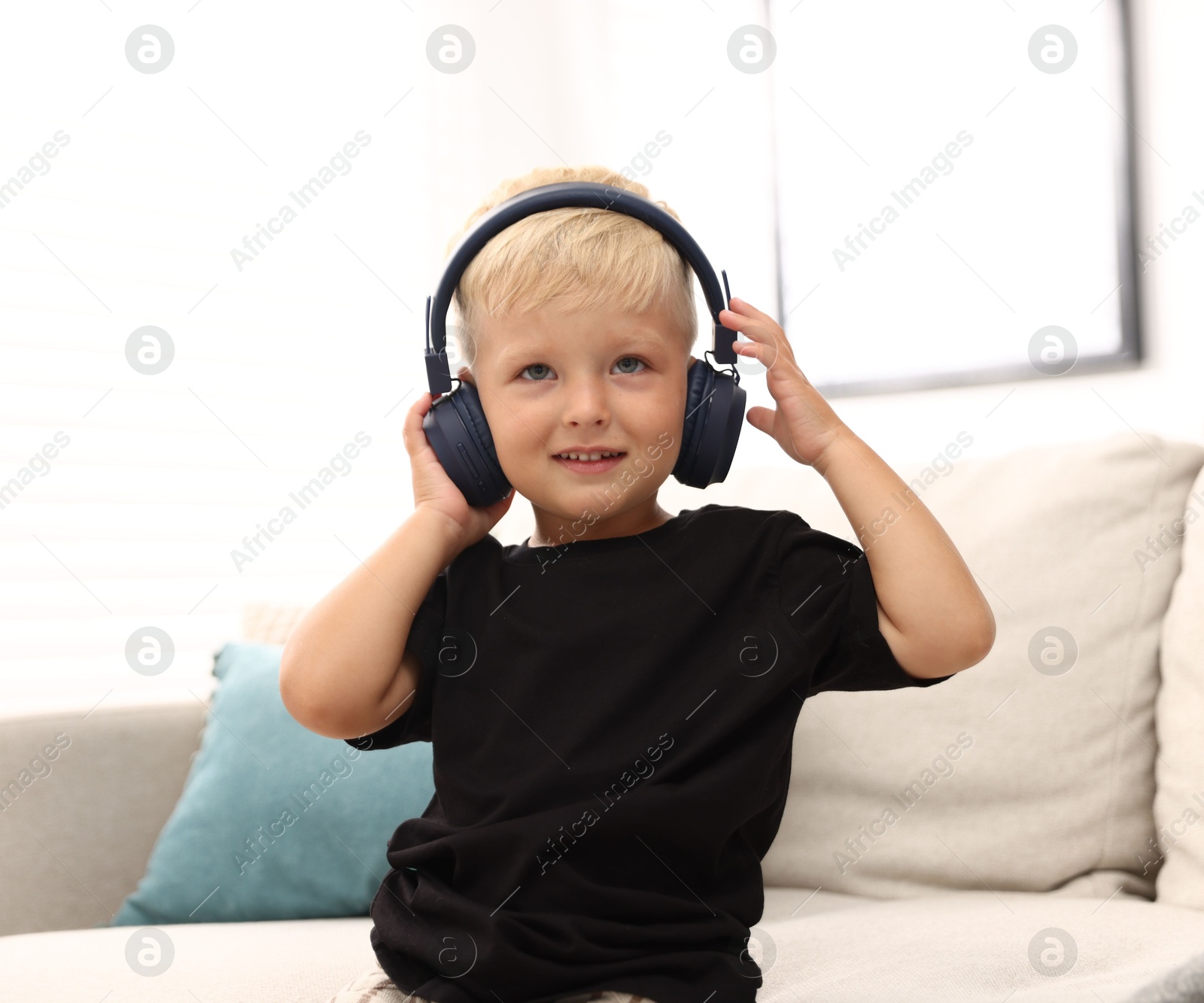 Cute little boy in headphones on sofa at home Photo of Cute little boy in headphones on sofa at home