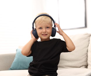 Photo of Cute little boy in headphones on sofa at home