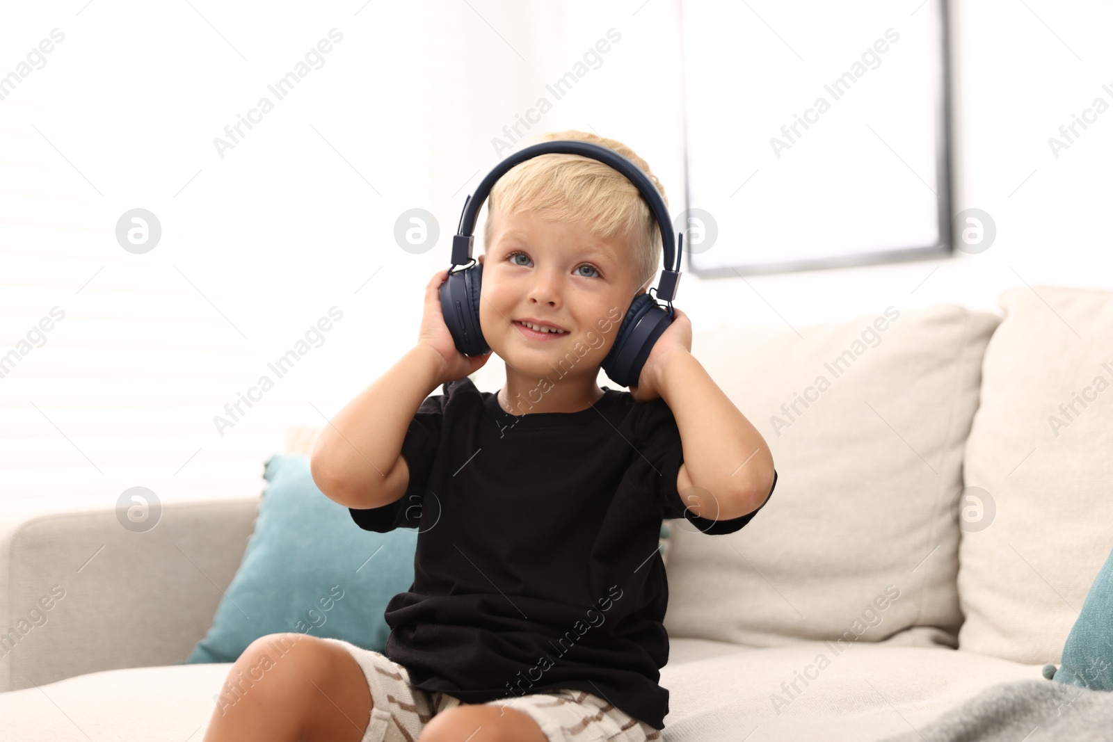 Photo of Cute little boy in headphones on sofa at home