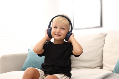 Photo of Cute little boy in headphones on sofa at home