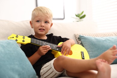 Photo of Cute little boy playing toy guitar on sofa at home
