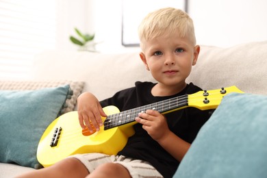 Photo of Cute little boy playing toy guitar on sofa at home
