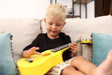 Photo of Cute little boy playing toy guitar on sofa at home
