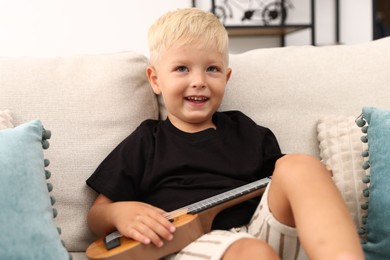 Photo of Cute little boy playing toy guitar on sofa at home