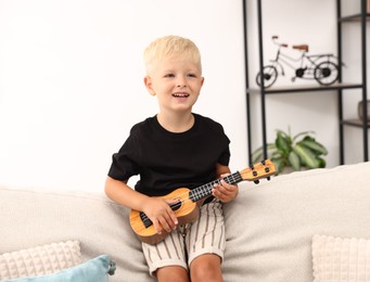 Photo of Cute little boy playing toy guitar on sofa at home