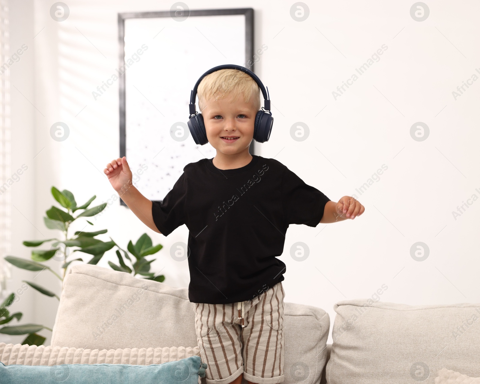 Photo of Cute little boy in headphones on sofa at home