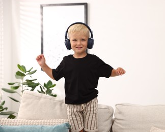 Photo of Cute little boy in headphones on sofa at home