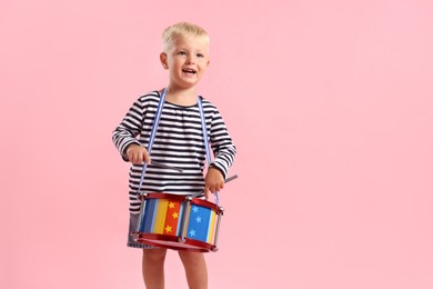 Photo of Cute little boy playing drum on pink background. Space for text